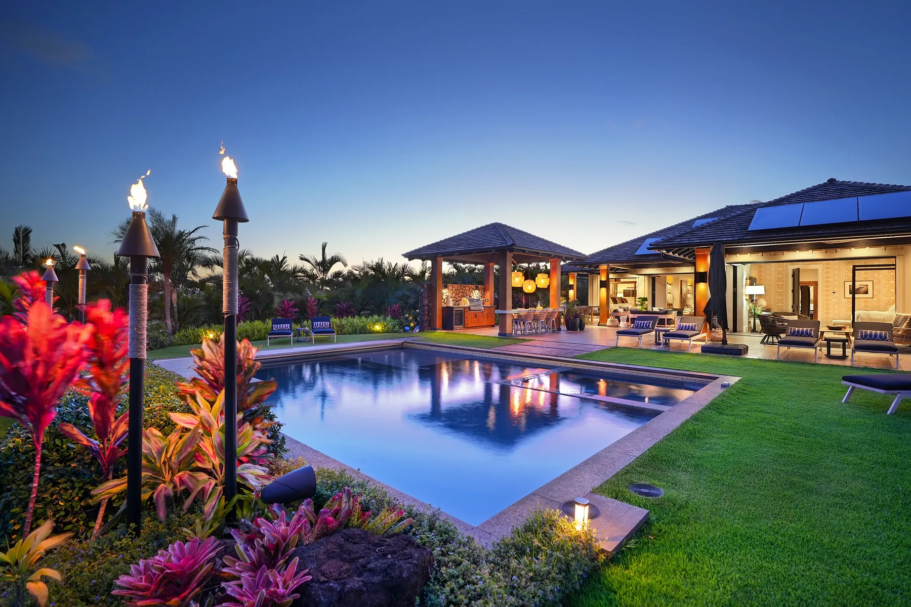 A landscaped outdoor pool sits beside a brightly lit single-story building at dusk.