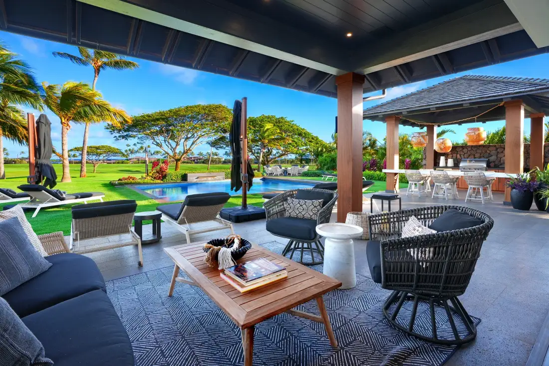 A covered outdoor lounge with seating overlooks a landscaped garden and pool.