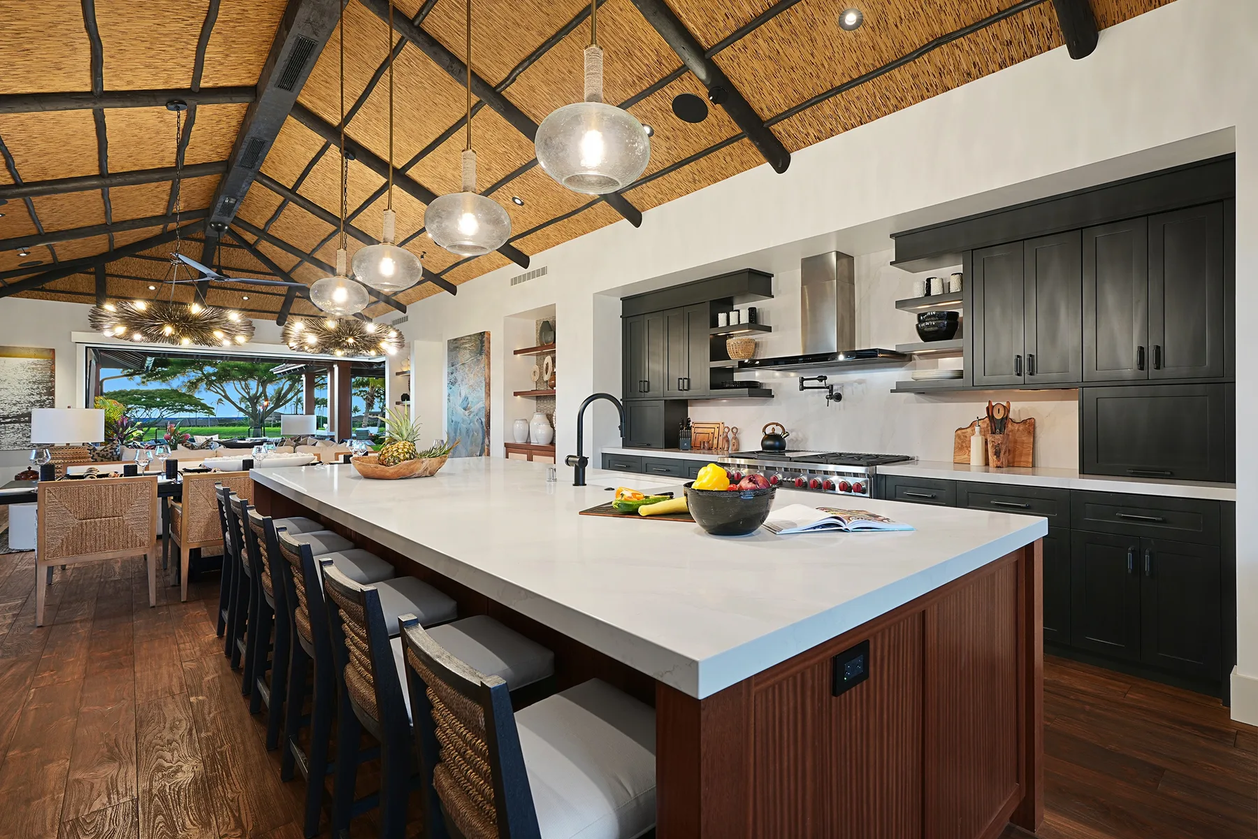 A spacious kitchen with a long island and dark cabinetry beneath a high exposed ceiling.