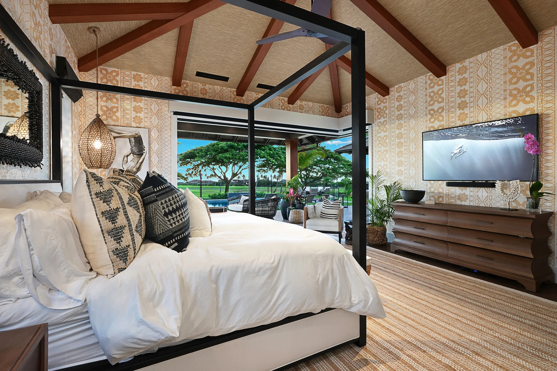 A bedroom with a canopy bed, patterned walls, and views of greenery through glass doors.