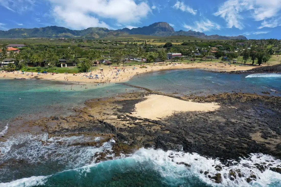 Aerial view of a sandy beach, rocky shoreline, and green mountains.