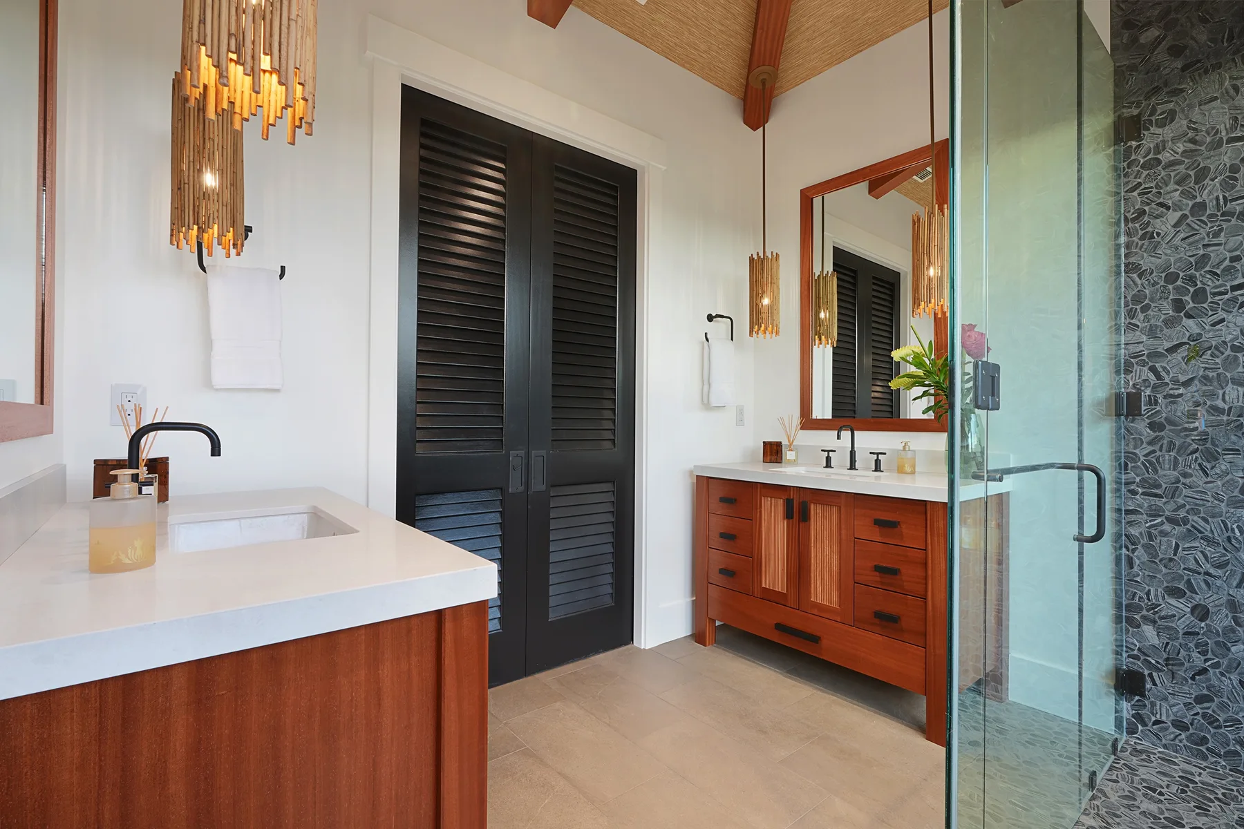 A modern bathroom with wood vanities, dark doors, and a glass shower.