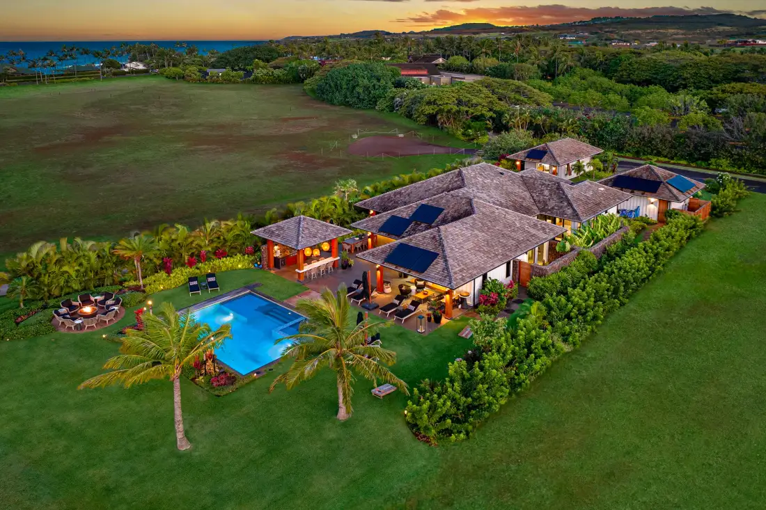 Aerial view of a landscaped property with a swimming pool and surrounding greenery at sunset.
