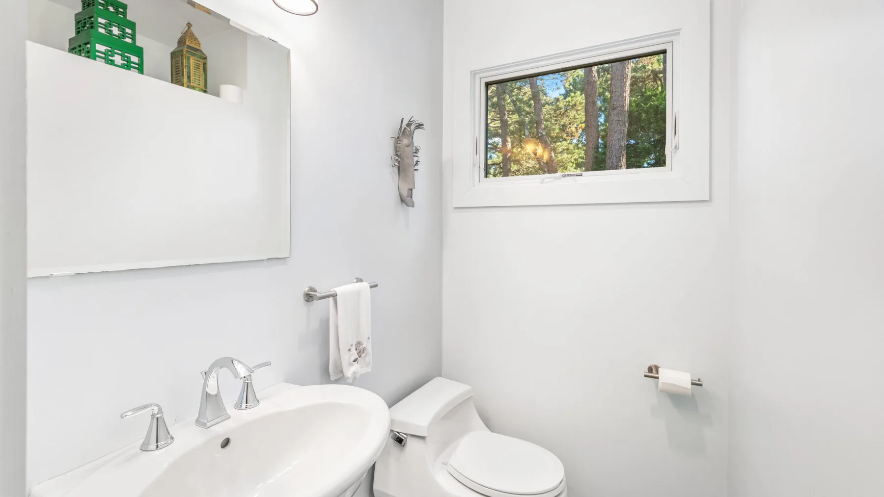 Un baño luminoso con lavabo, inodoro y una ventana con vista a los árboles.
