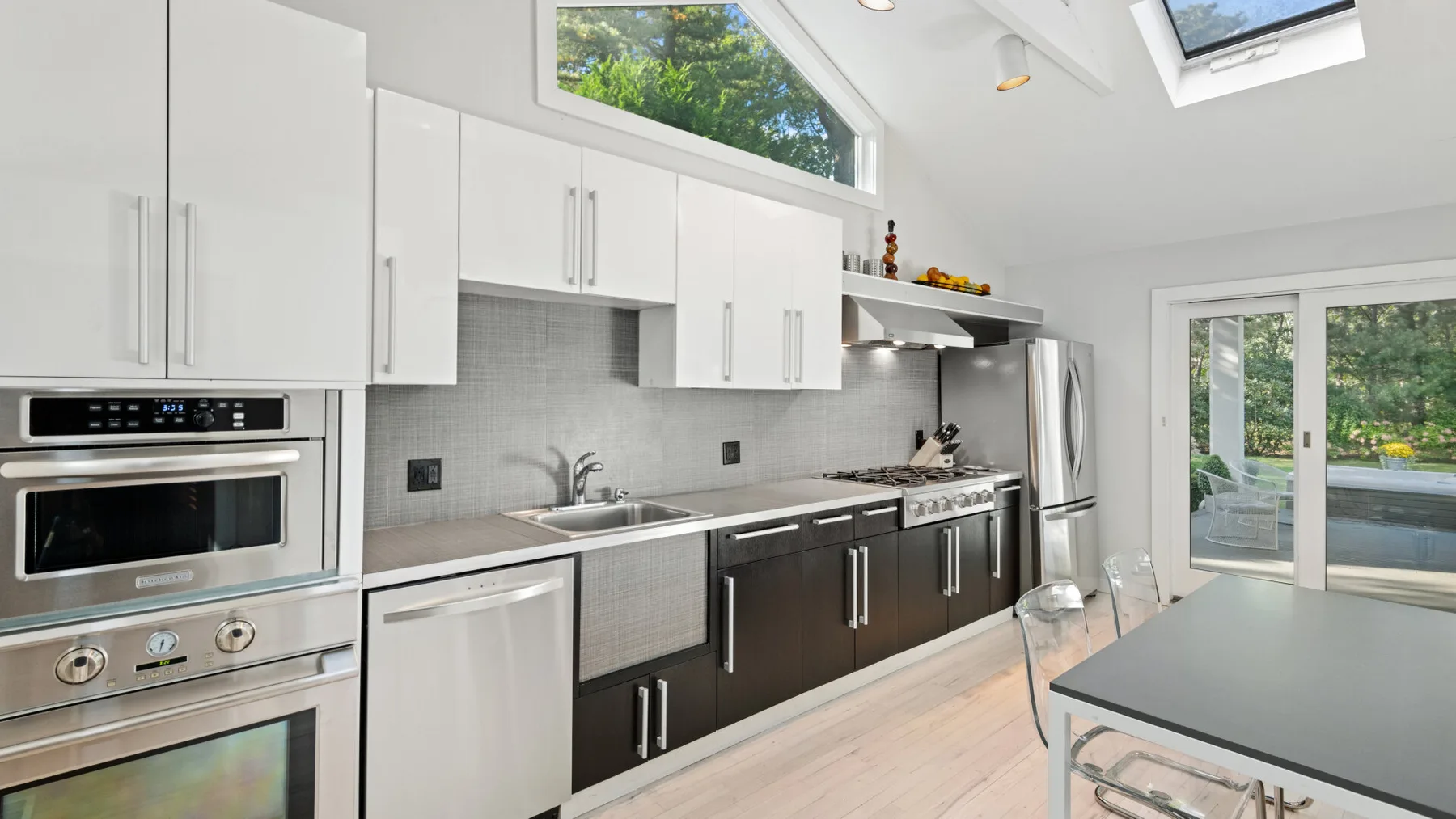 Una cocina luminosa con gabinetes inferiores oscuros y un refrigerador de acero inoxidable.