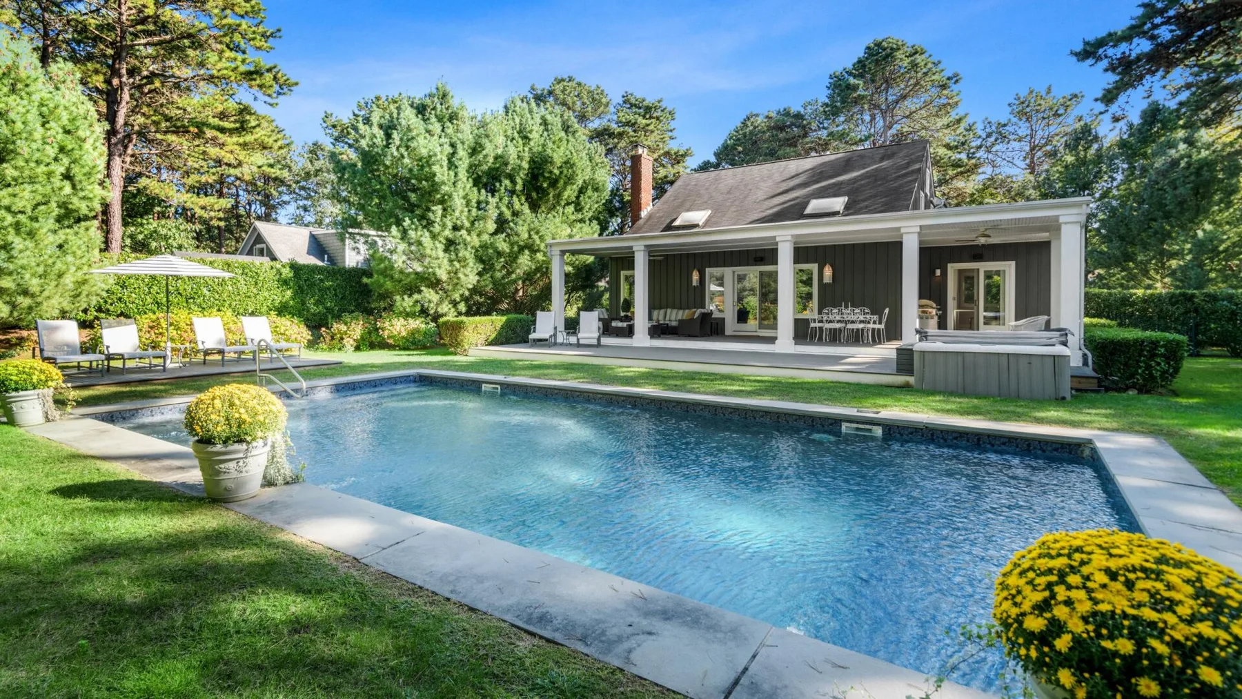 Piscina exterior junto a una casa, con un patio cubierto y vegetación alrededor.
