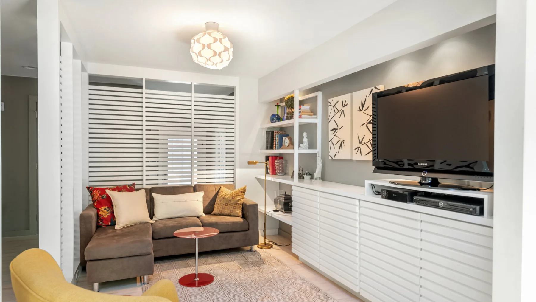 Una sala de estar con un sofá, un televisor y armarios blancos.