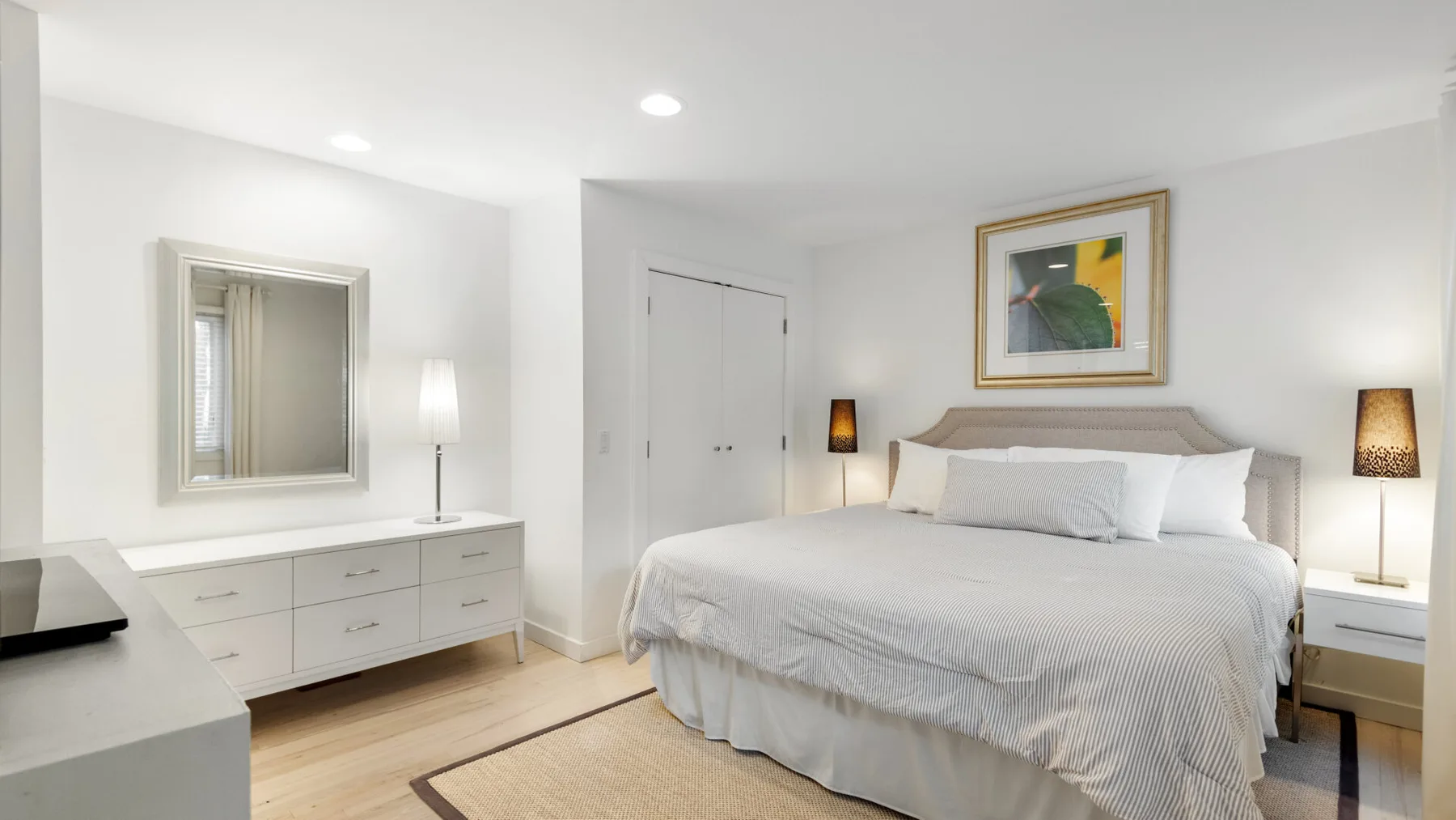 Un dormitorio luminoso tiene una cama bien tendida, mesitas de noche y una cómoda con espejo.