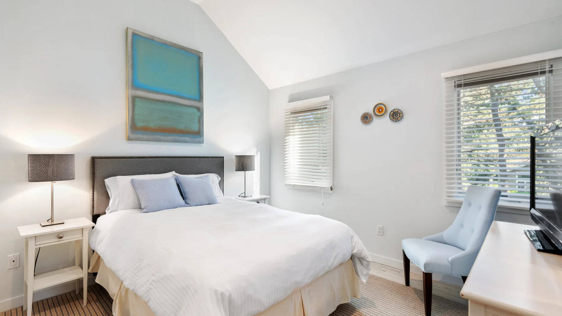 Un dormitorio luminoso con una cama grande, mesas de noche y ventanas con persianas.