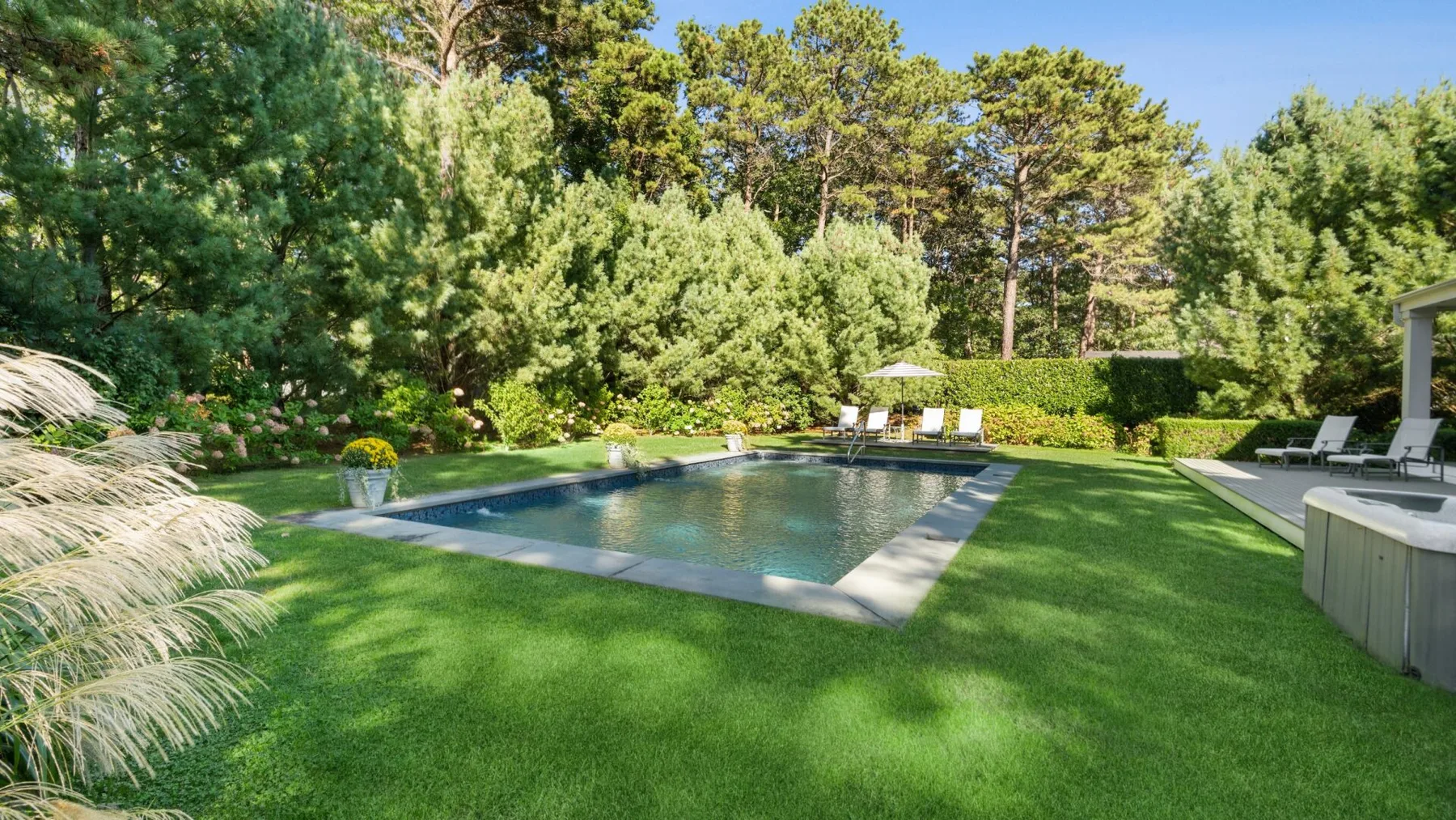 Una piscina en un jardín está rodeada de césped verde y árboles.