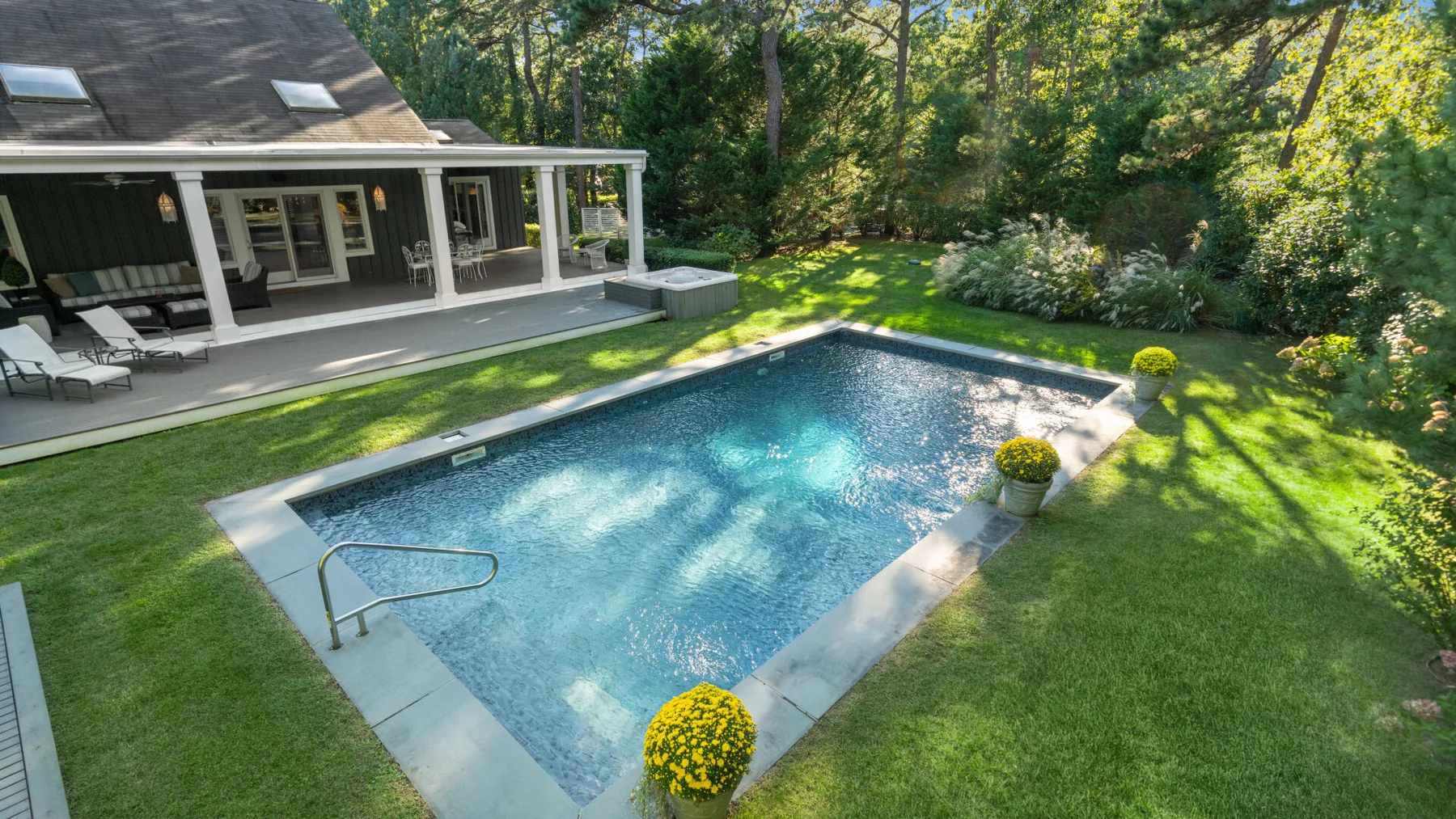 Una piscina en el patio está junto al césped y una casa.