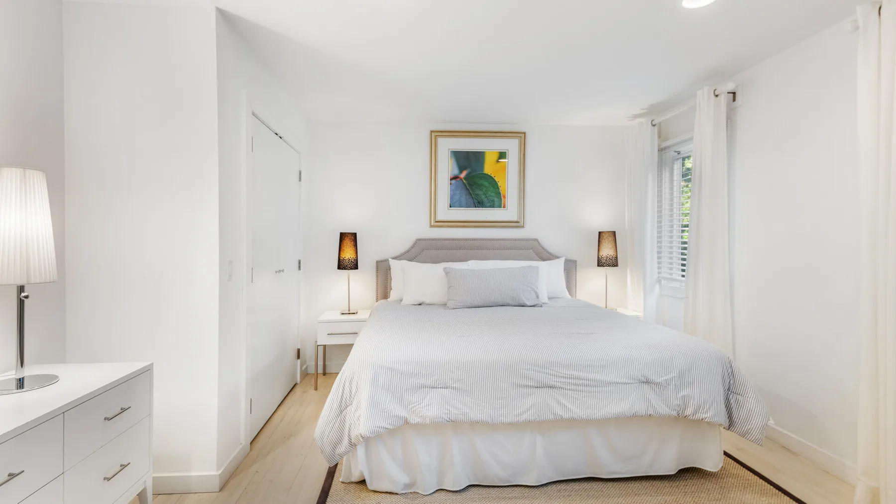 Un dormitorio luminoso con una cama, mesitas de noche y un cuadro sobre el cabecero.