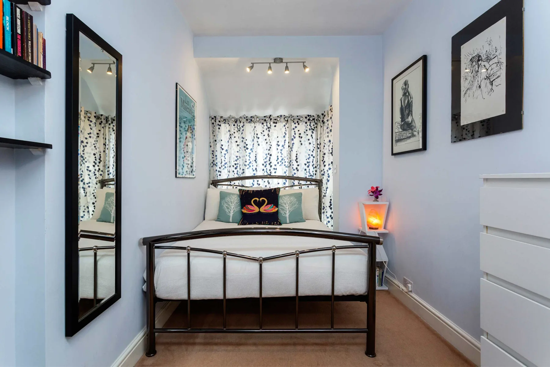 A bedroom with a metal-framed bed, patterned curtains, and framed wall art.