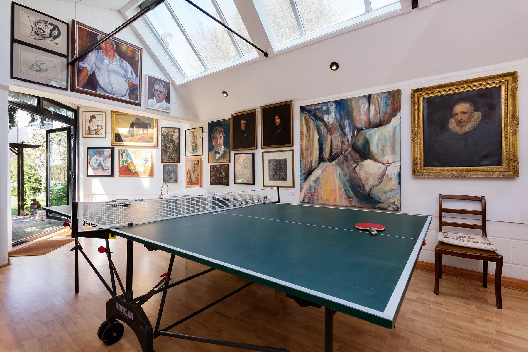 A table tennis table stands in a bright room filled with framed paintings.