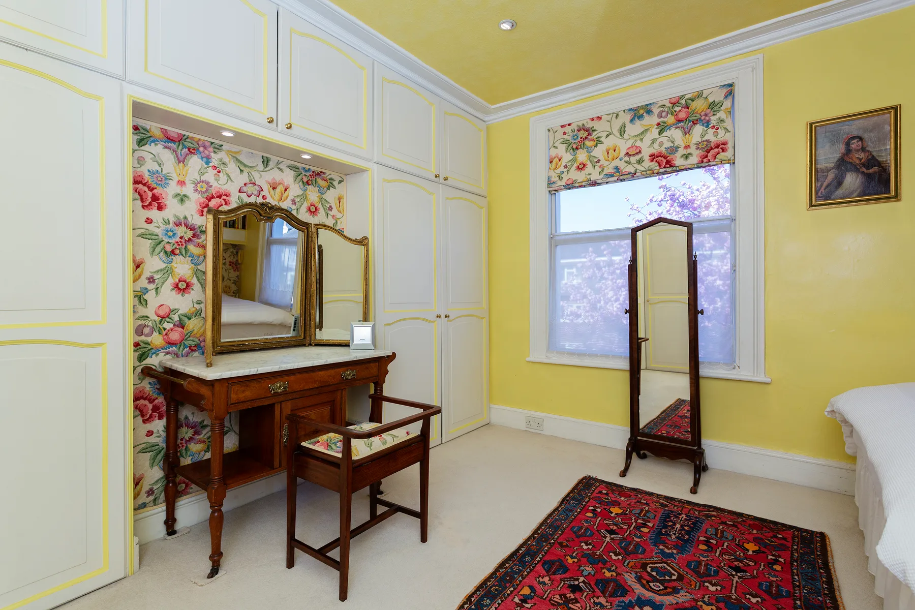 A bedroom dressing area with a wooden vanity, standing mirror, and patterned rug.