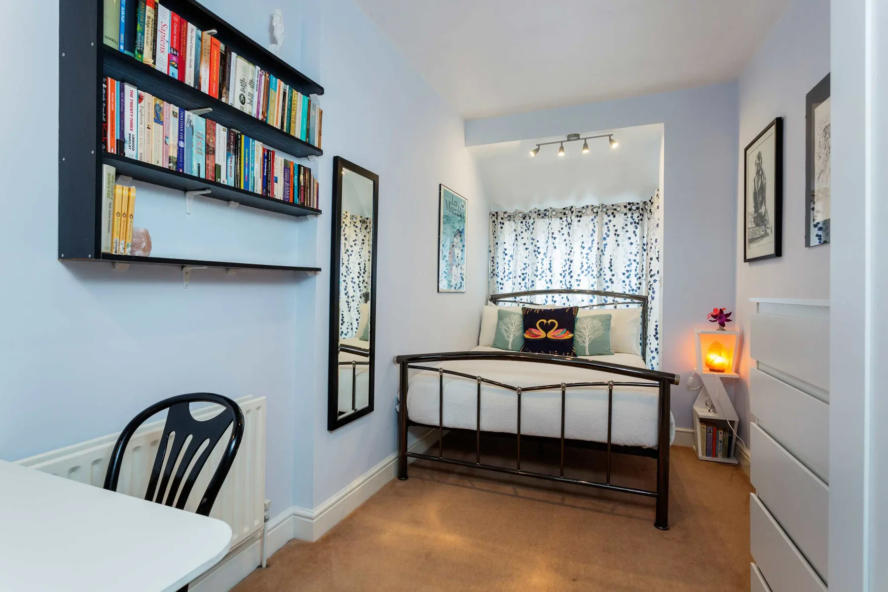 A bedroom with a bed beneath patterned curtains and wall-mounted bookshelves.