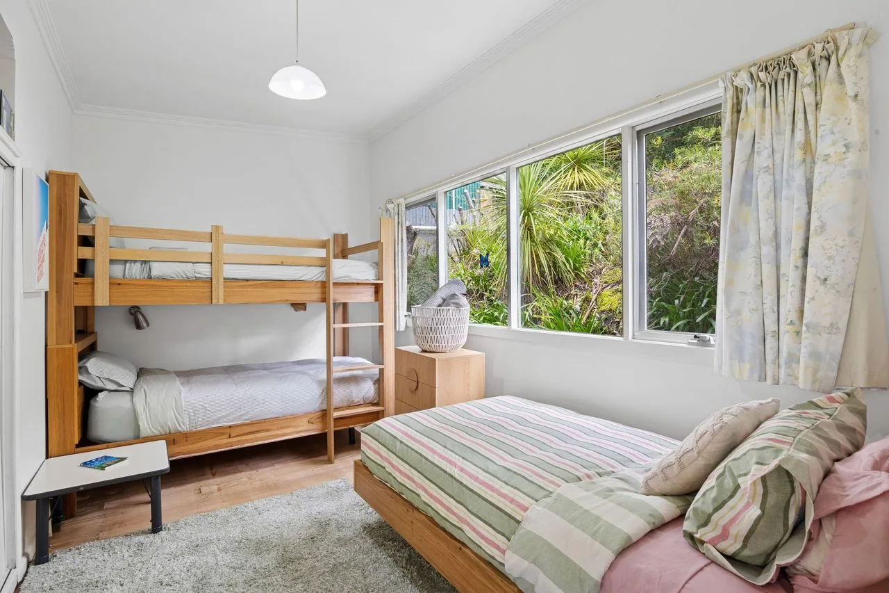 Un dormitorio luminoso con literas y una cama junto a grandes ventanas.