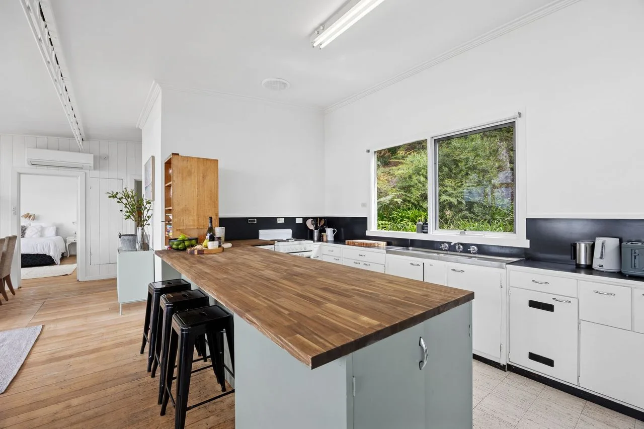 Una cocina luminosa con una isla larga de madera y ventanas grandes.