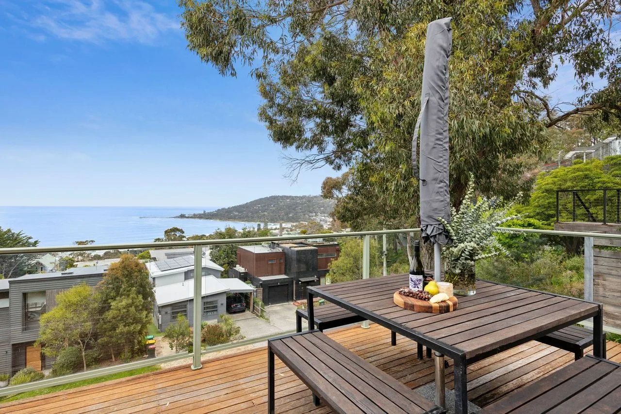 Una terraza de madera con asientos al aire libre da a la costa y a casas cercanas.