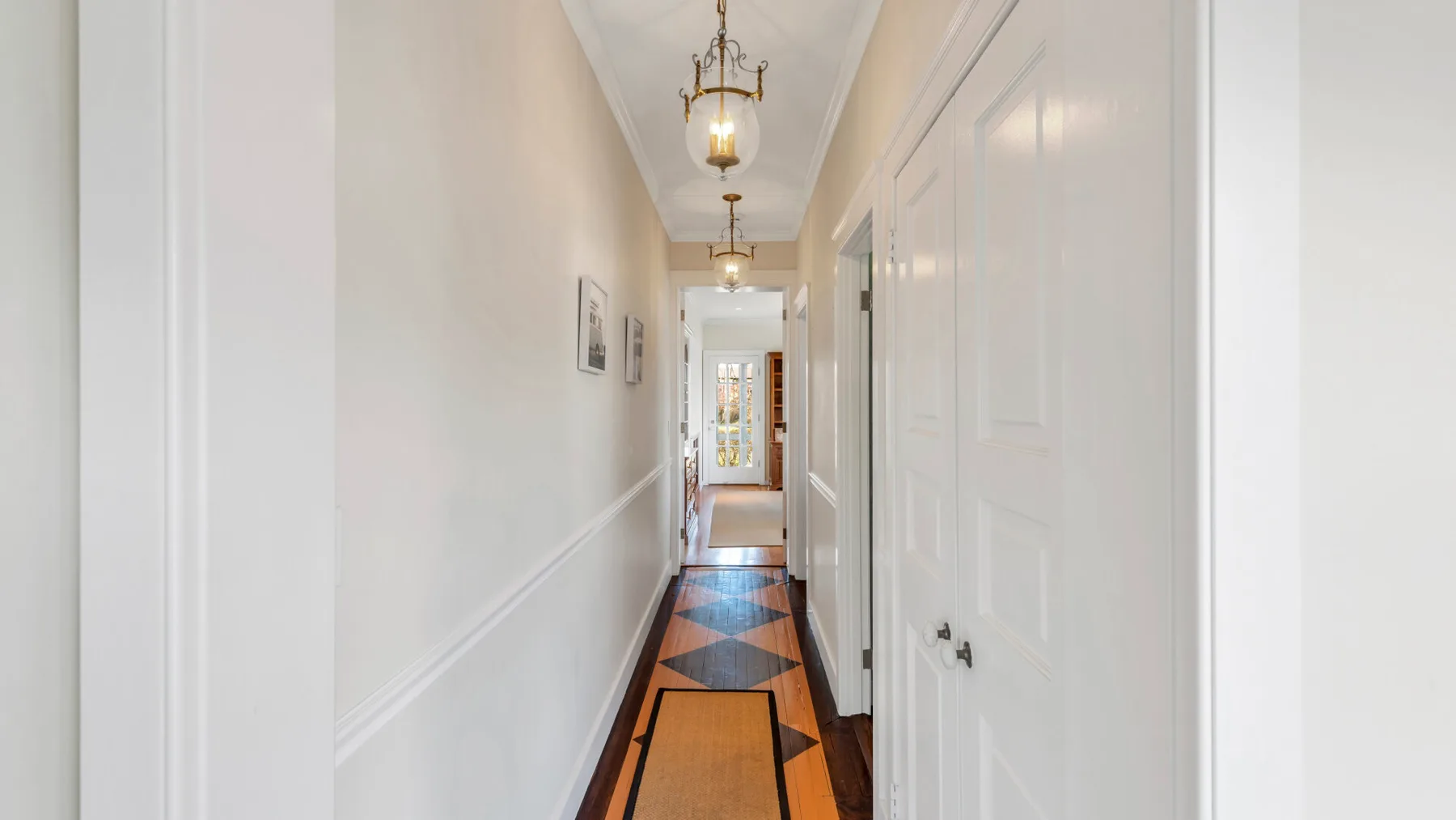 A narrow hallway with white walls, closed doors, and patterned flooring.