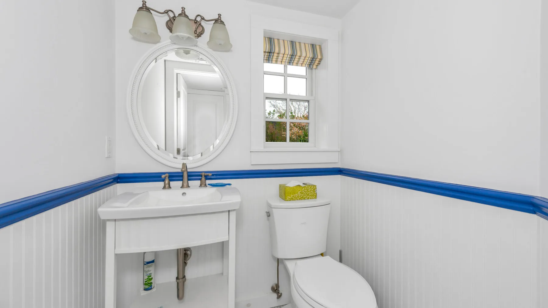 Un baño luminoso con lavabo blanco, espejo redondo y ventana.