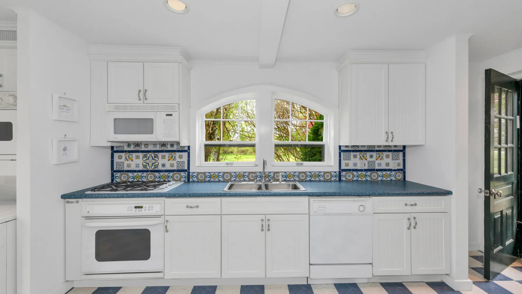Una cocina blanca y luminosa con una encimera larga, horno integrado y ventanas arqueadas.