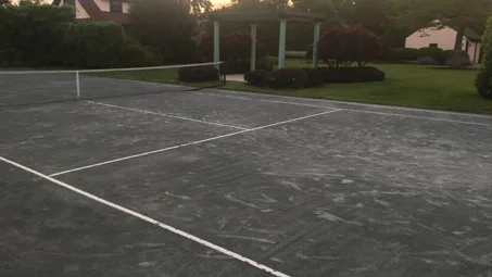 Una cancha de tenis al aire libre con una red y una pequeña zona cubierta cercana.