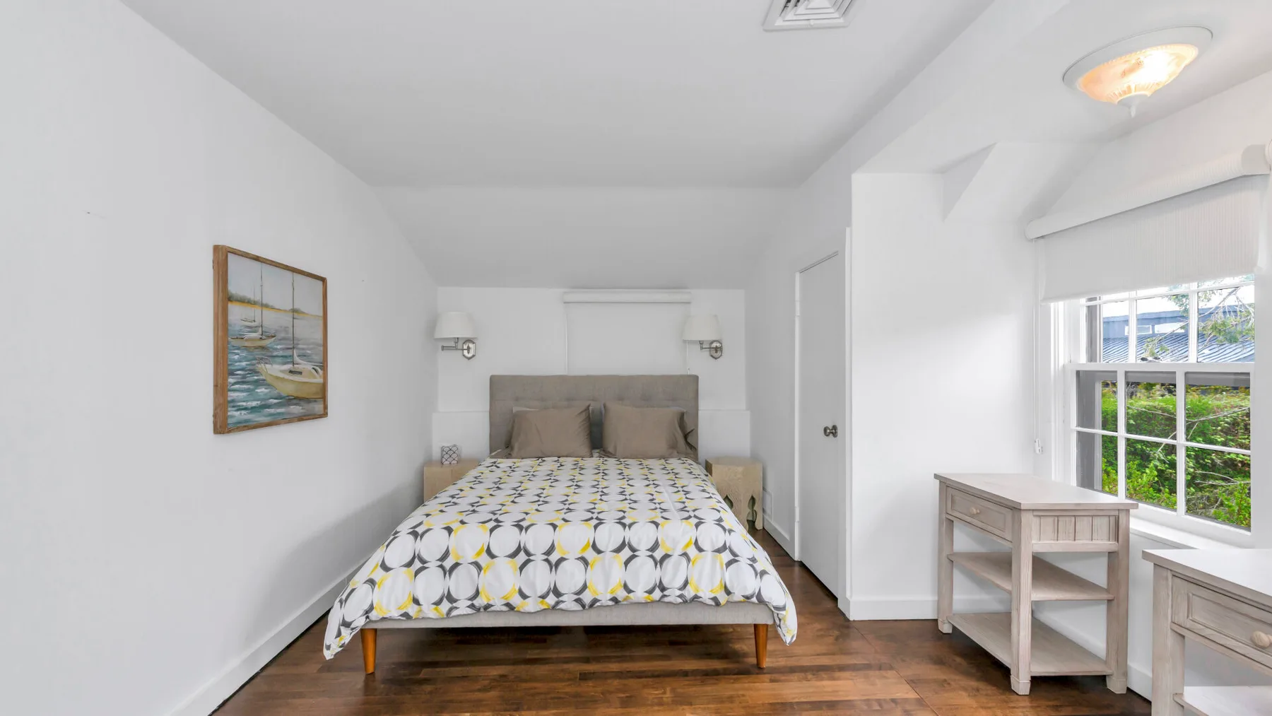 Un dormitorio con una cama y un escritorio pequeño junto a la ventana.
