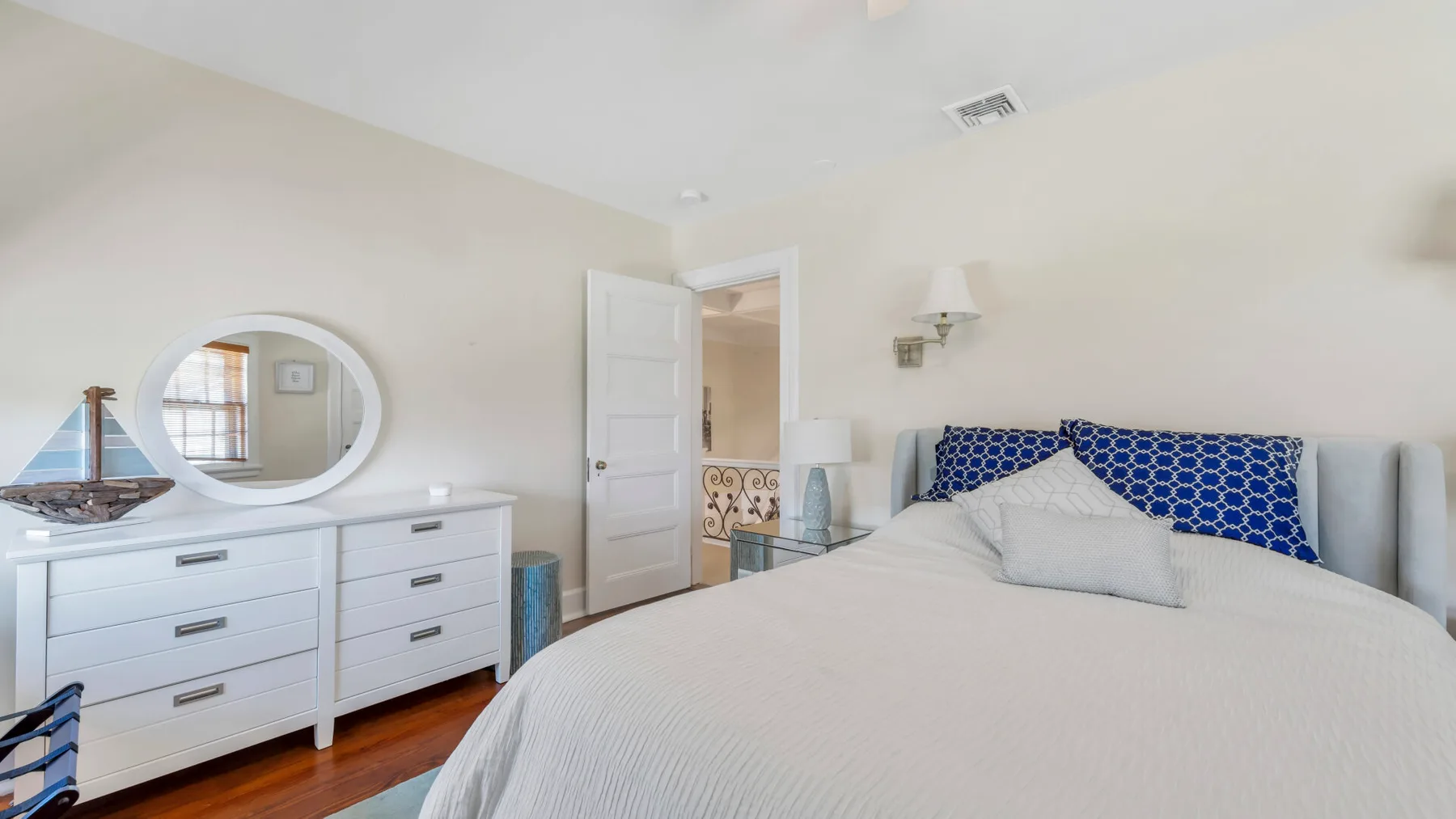 Un dormitorio con una cama grande, una cómoda blanca y un espejo redondo en la pared.
