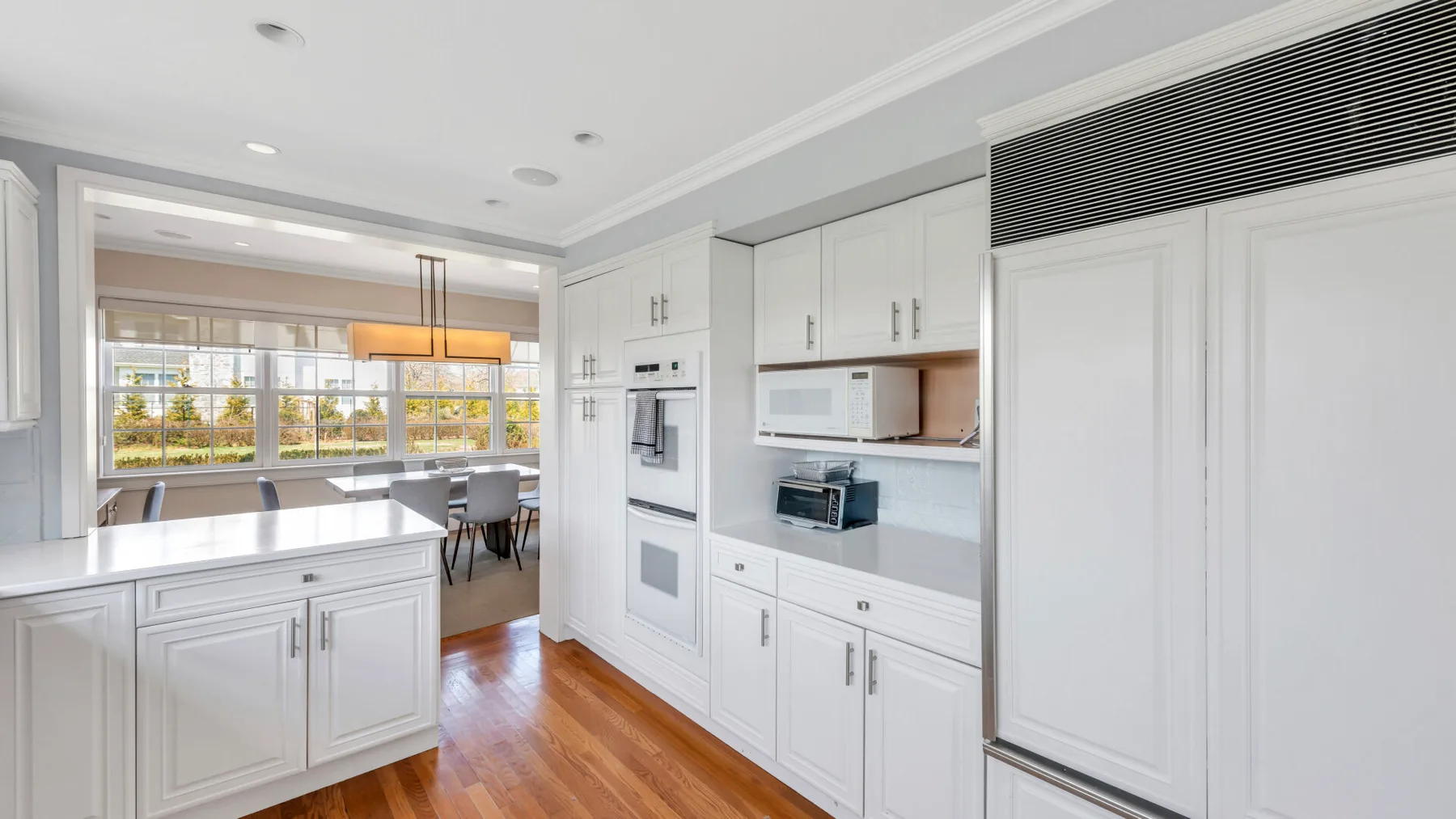 Una cocina blanca y luminosa con electrodomésticos integrados y un comedor al fondo.