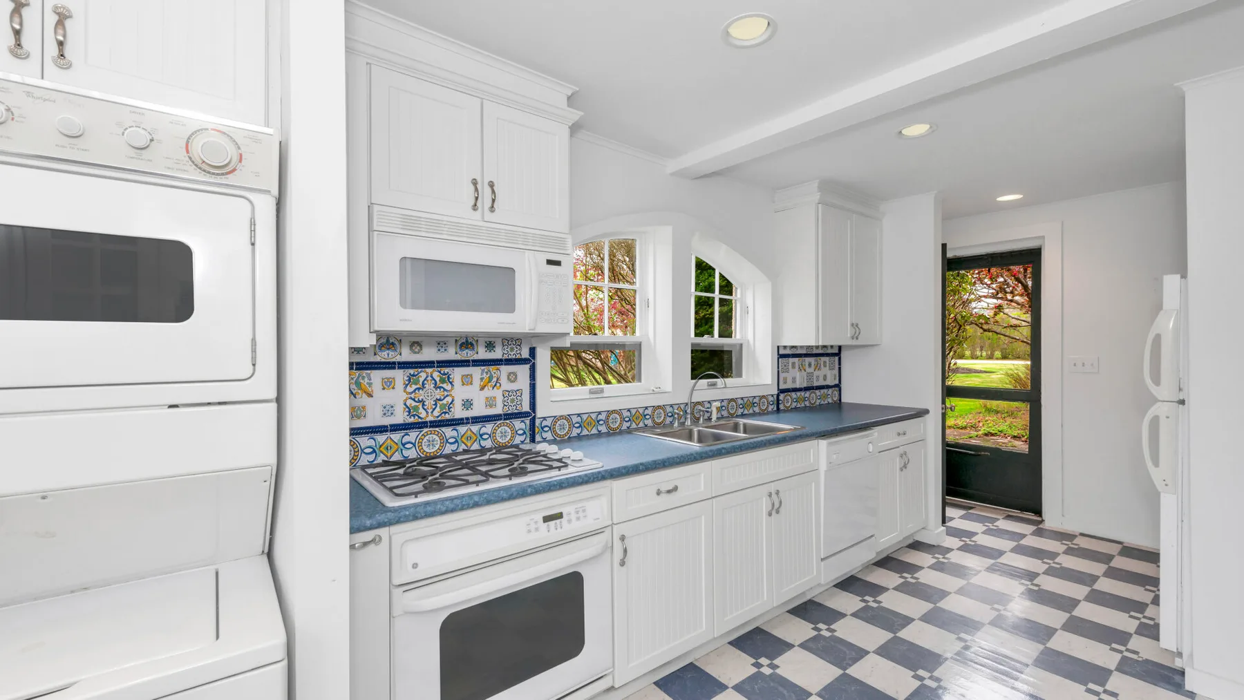 Una cocina luminosa con gabinetes blancos, azulejos estampados y piso de cuadros.