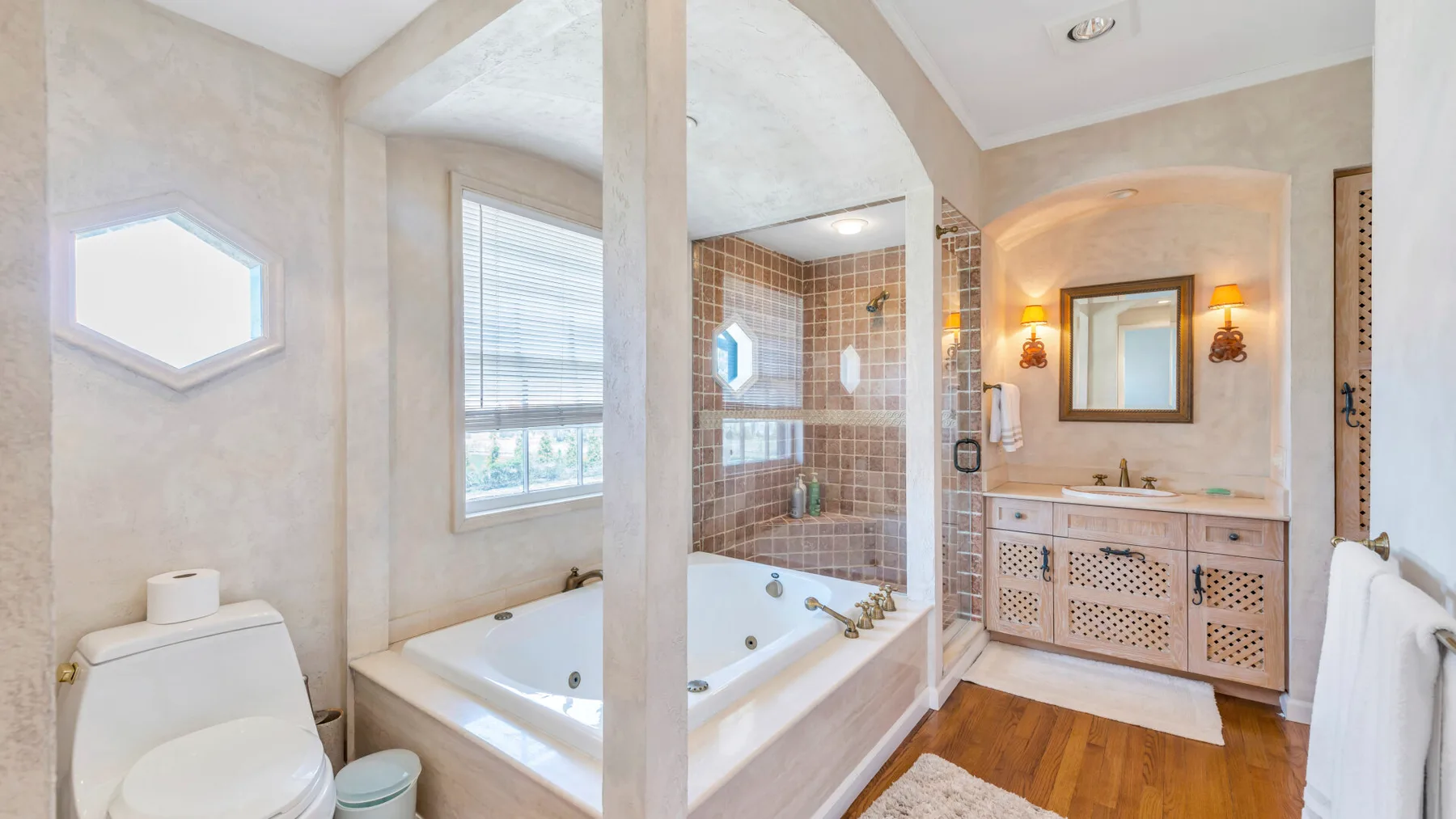 Un baño con bañera, tocador con lavabo y suelo de madera.
