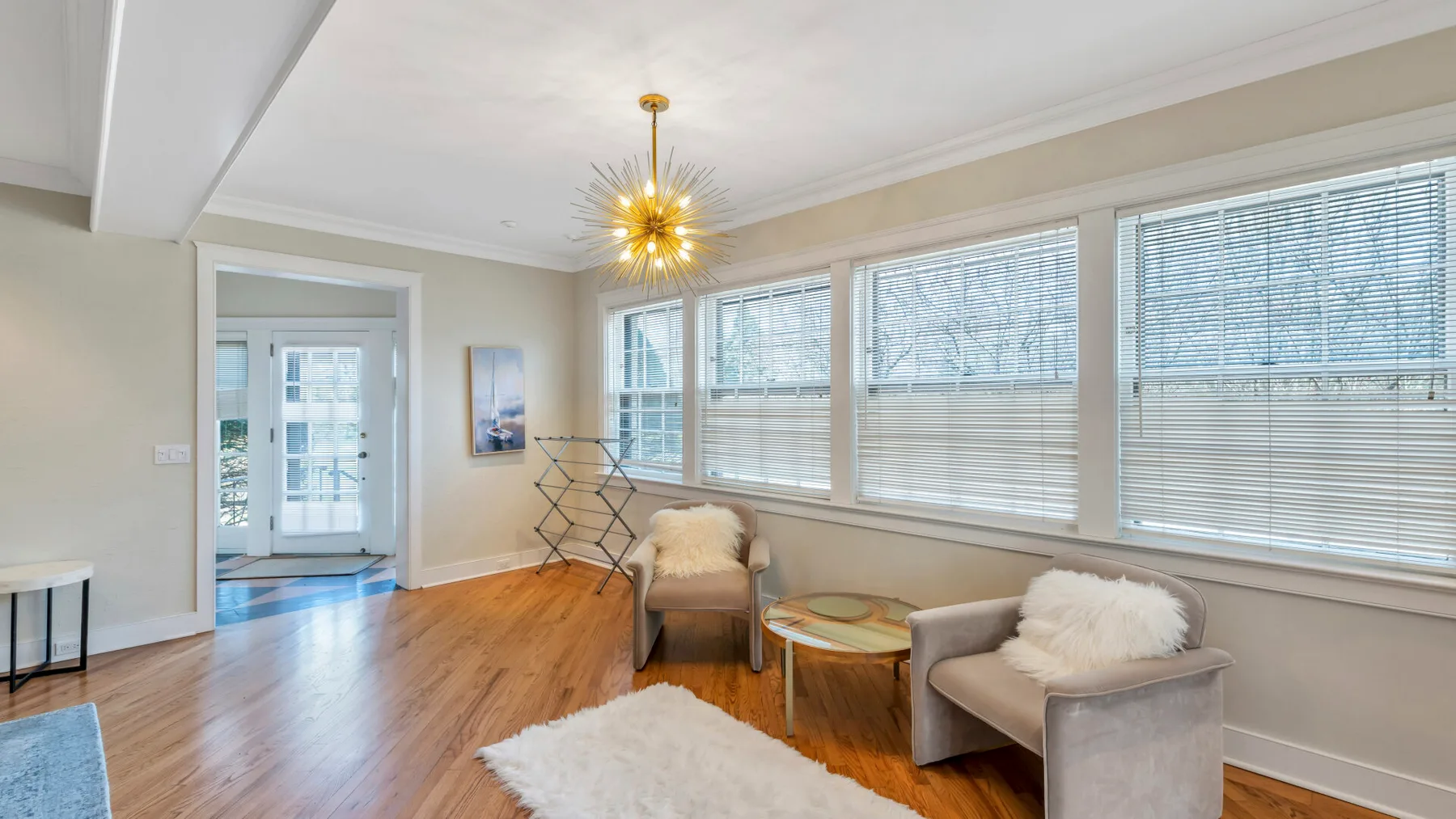 A bright sitting room has wide windows, wood flooring, and two upholstered seats.