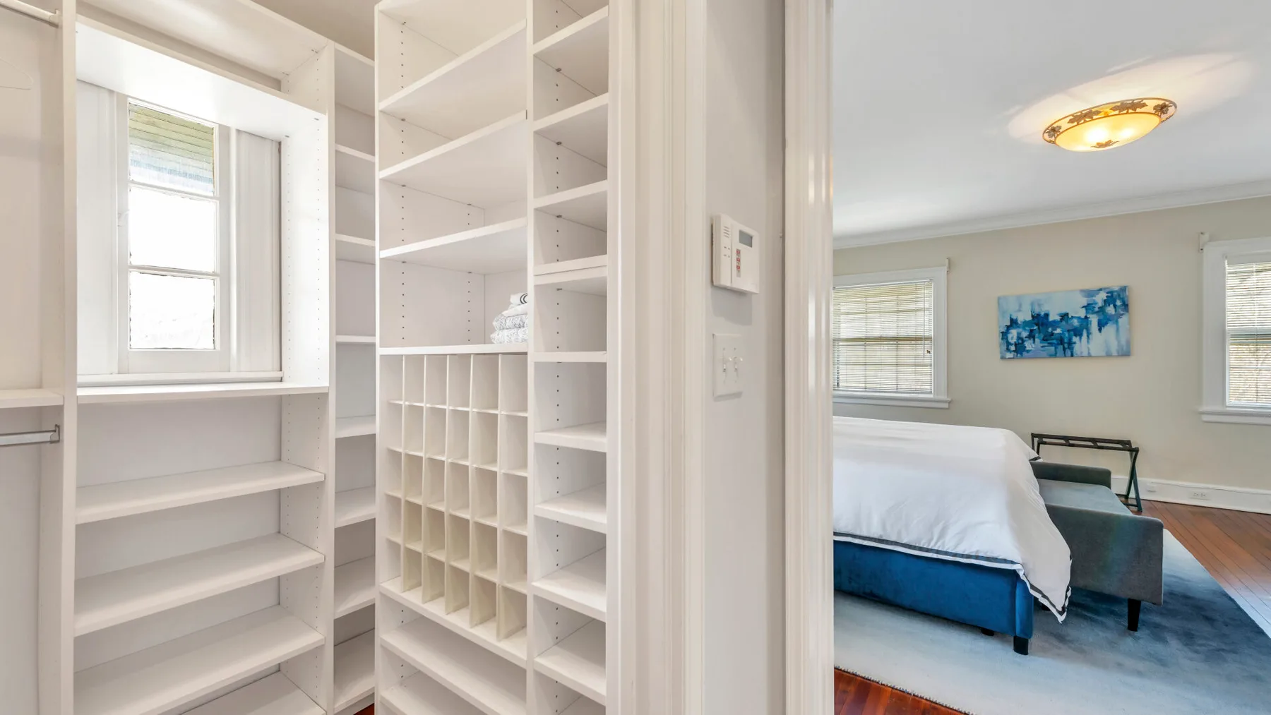 Estanterías blancas empotradas dan a un dormitorio con una cama azul y arte en la pared.