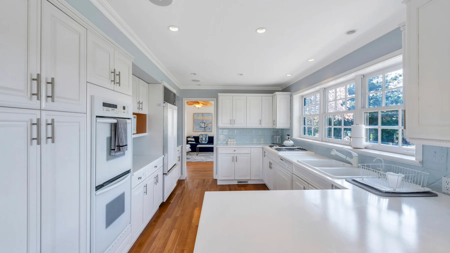 Una cocina luminosa con gabinetes blancos, una isla grande y ventanas a lo largo de una pared.
