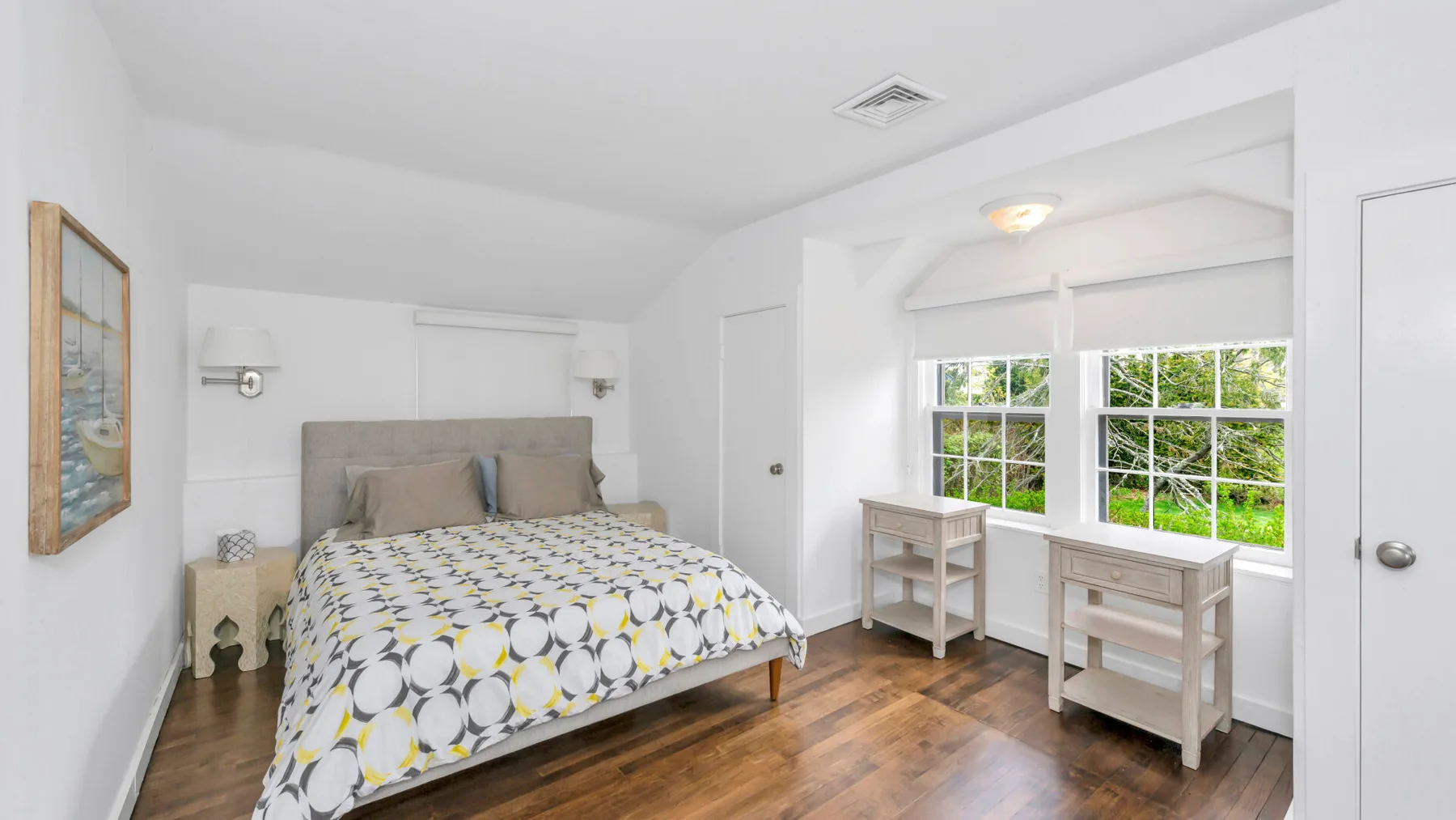Un dormitorio luminoso con una cama y un rincón junto a la ventana con mesitas.