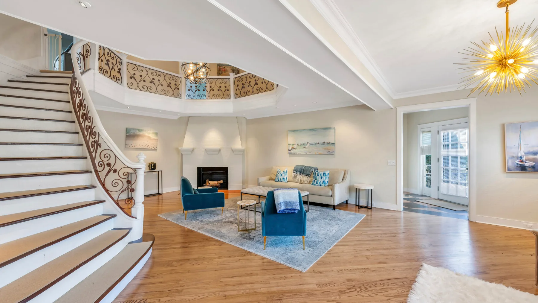 A bright living room with a curved staircase and seating around a fireplace.