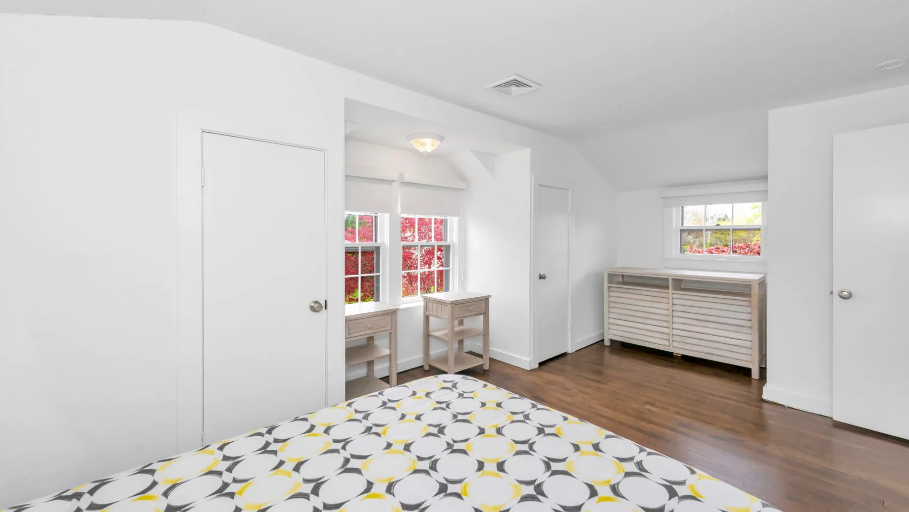 Un dormitorio con una colcha estampada, ventanas y suelo de madera.