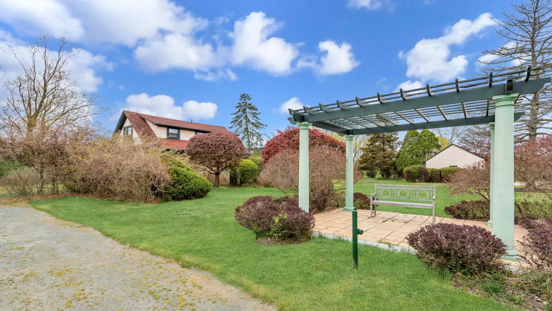 Un jardín ajardinado con pérgola, zona de estar pavimentada y césped.