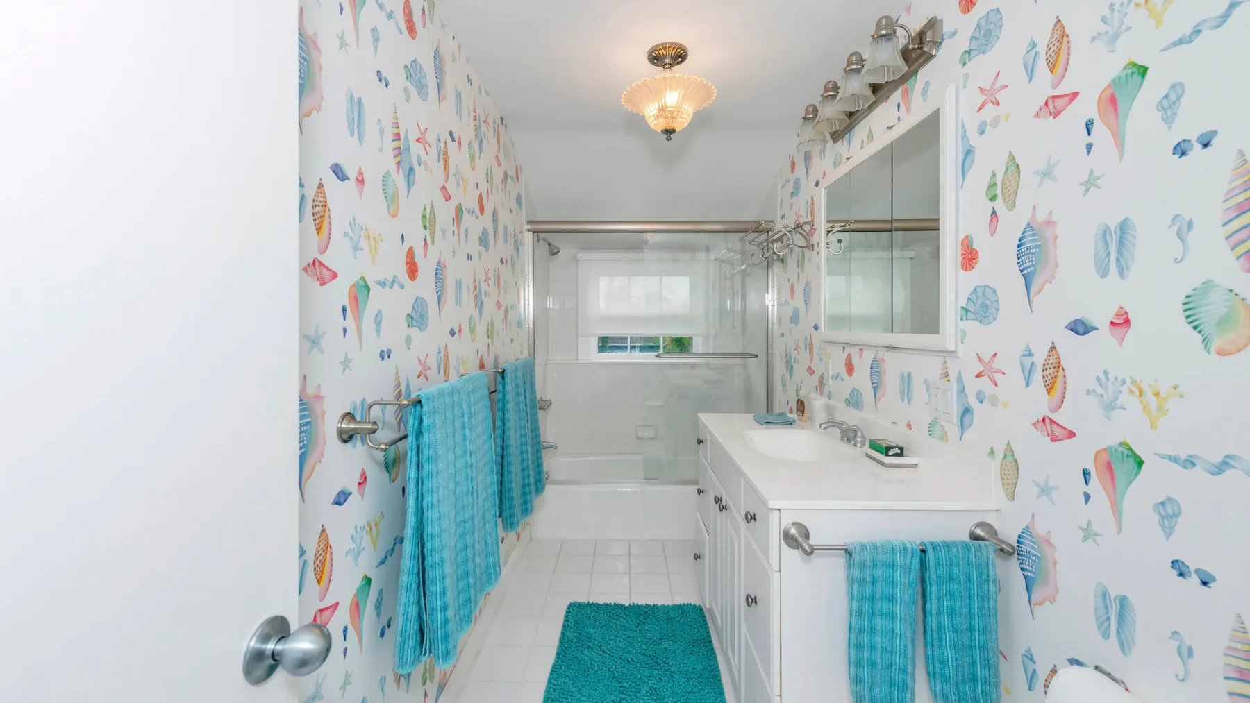Un baño colorido con paredes estampadas, un lavabo y toallas turquesas.