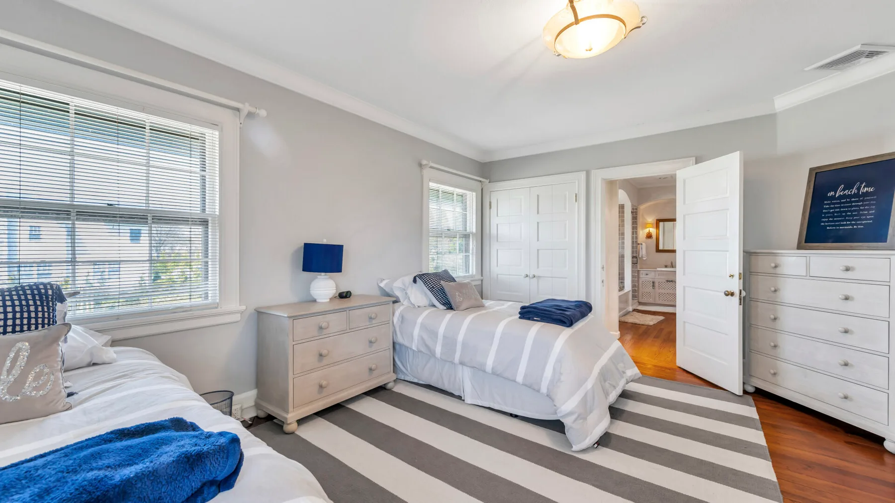 Un dormitorio luminoso con dos camas, ropa de cama a rayas y una cómoda.