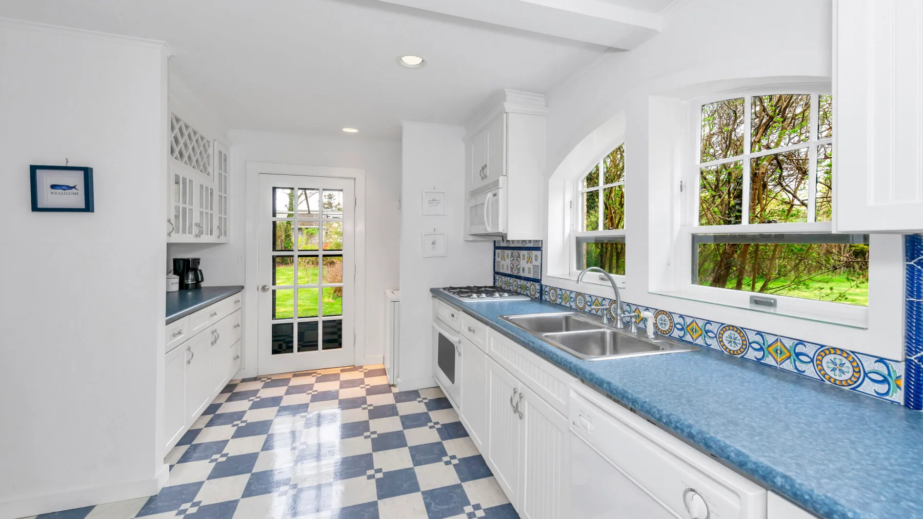 Una cocina blanca y luminosa con encimeras azules y suelo de cuadros.