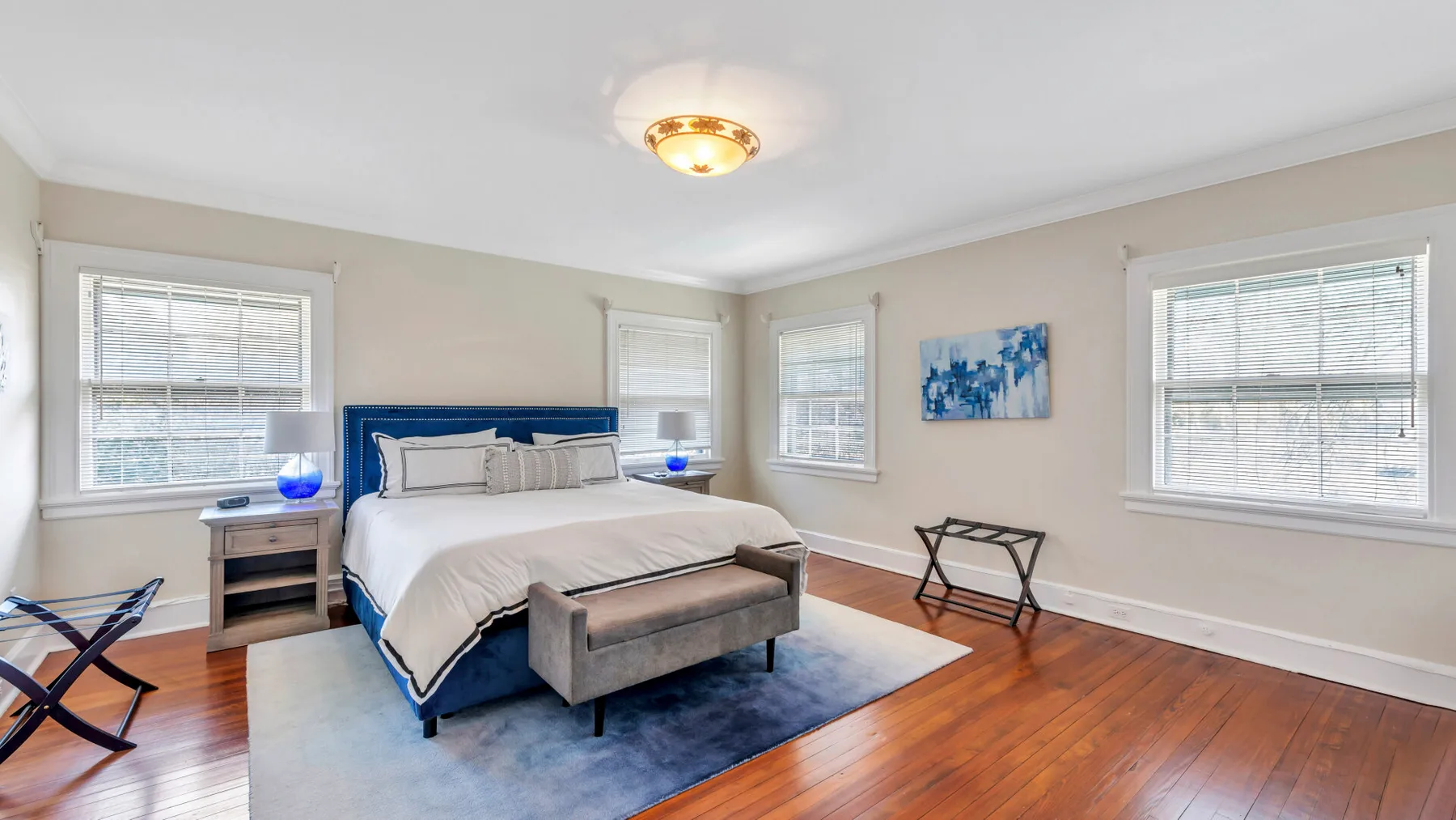 Un dormitorio luminoso con una cama, suelo de madera y varias ventanas.