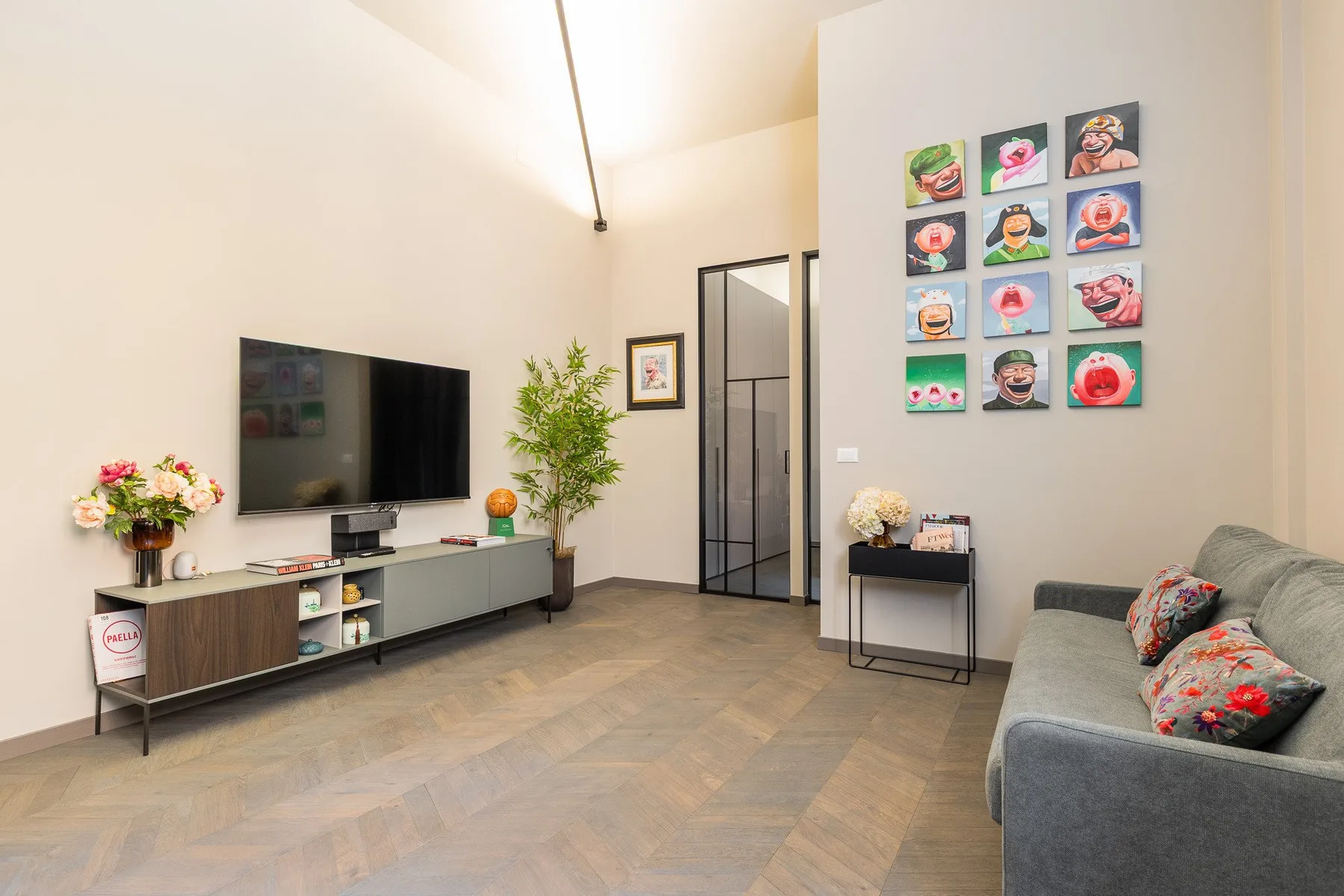 Una sala de estar luminosa con televisor, arte en la pared y asientos grises.