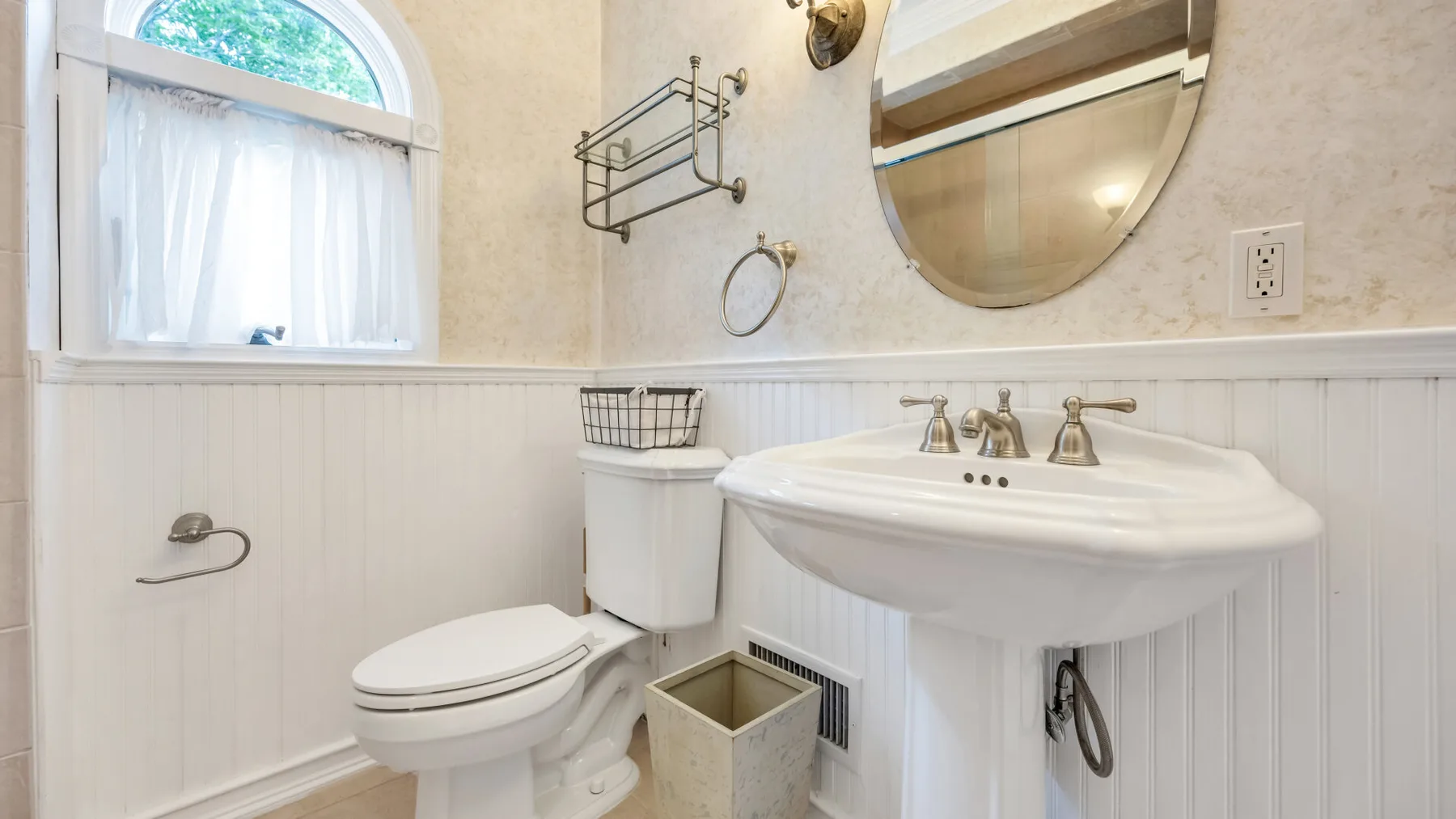 Un baño con lavabo, inodoro y una ventana arqueada.