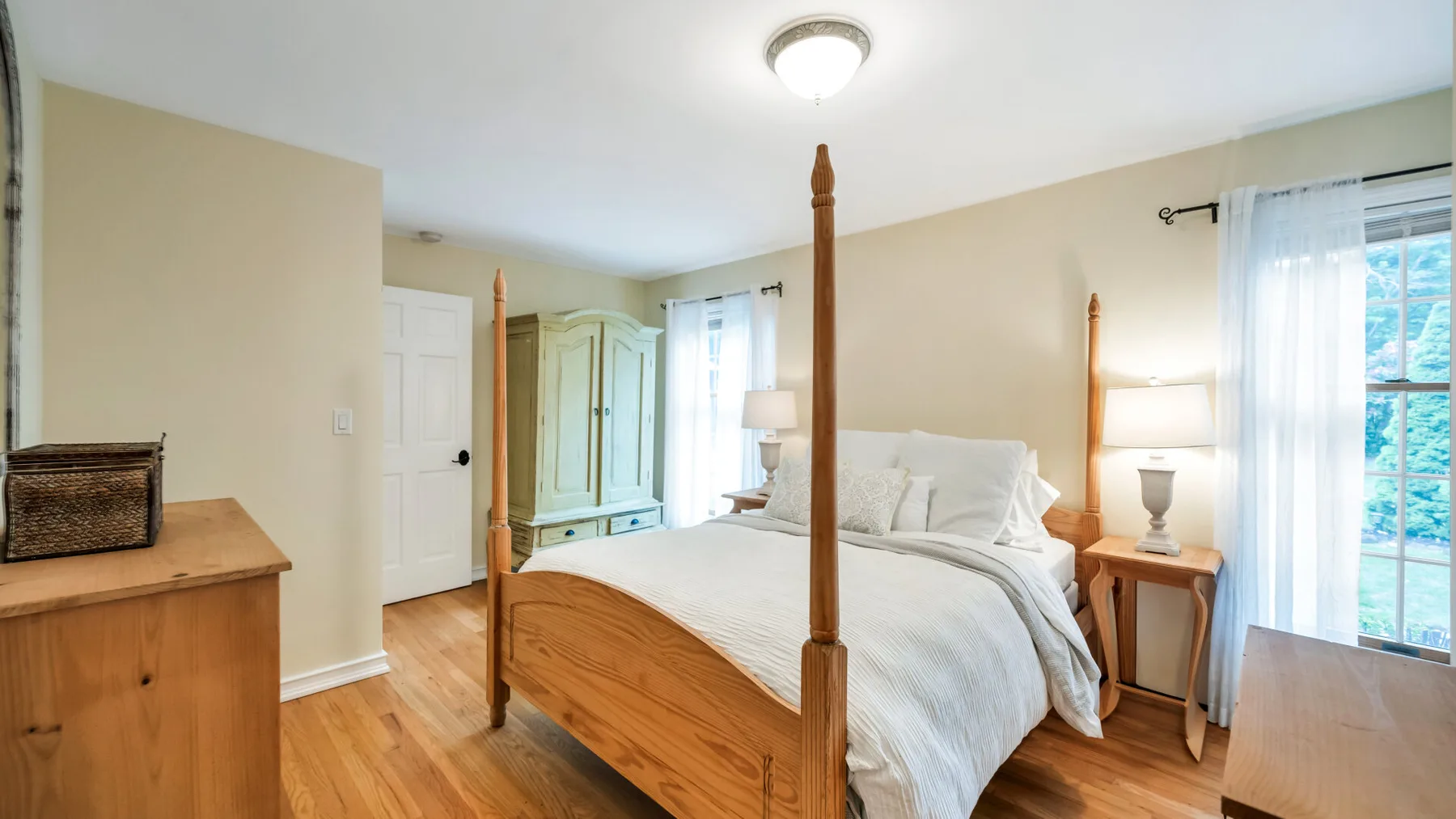 Un dormitorio con una cama de madera, mesillas y una ventana con cortinas transparentes.