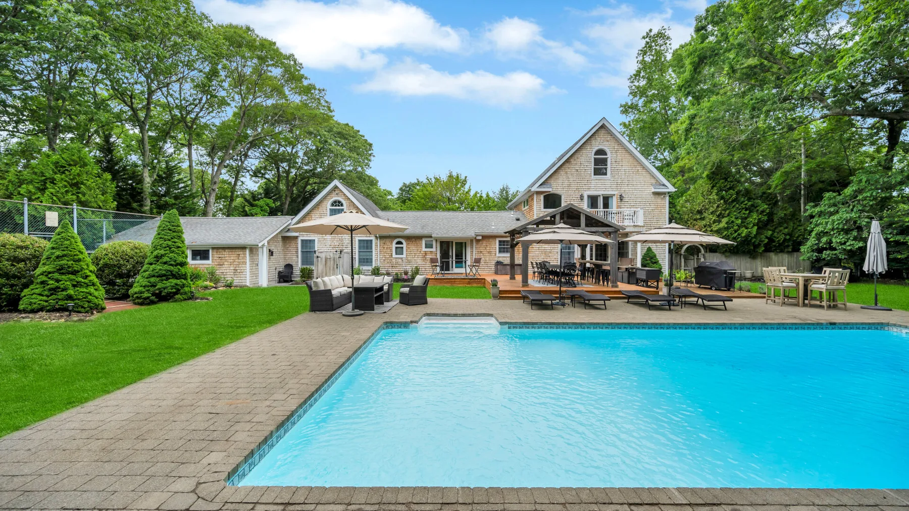 Una piscina exterior está junto a una casa grande y un césped ajardinado.