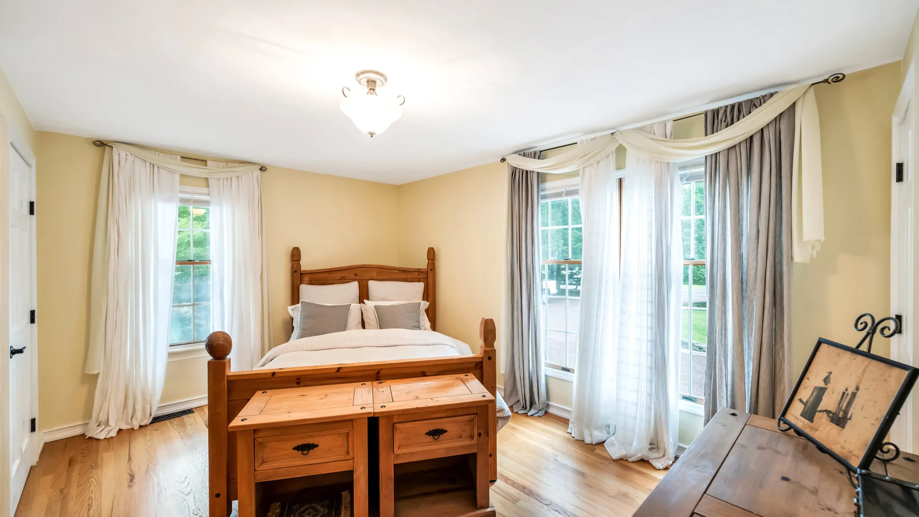 Un dormitorio luminoso con una cama de madera y ventanas altas con cortinas.