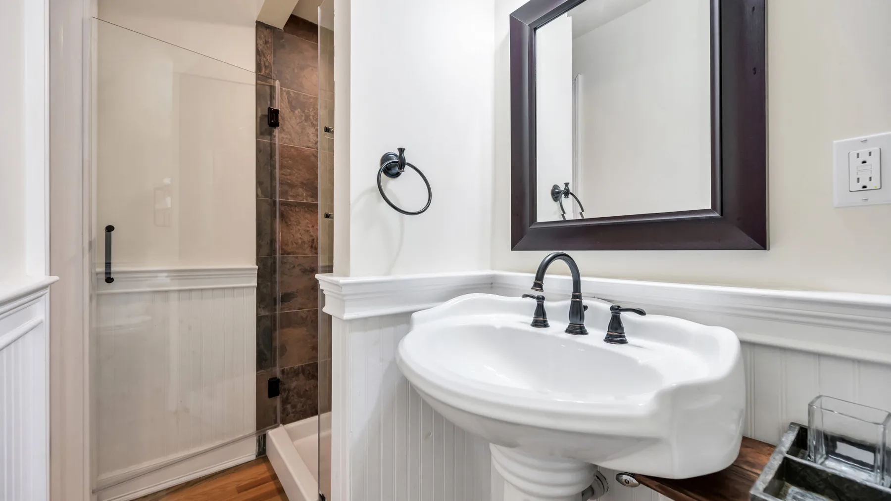 Un lavabo de baño y un espejo están junto a una ducha con mampara de vidrio.