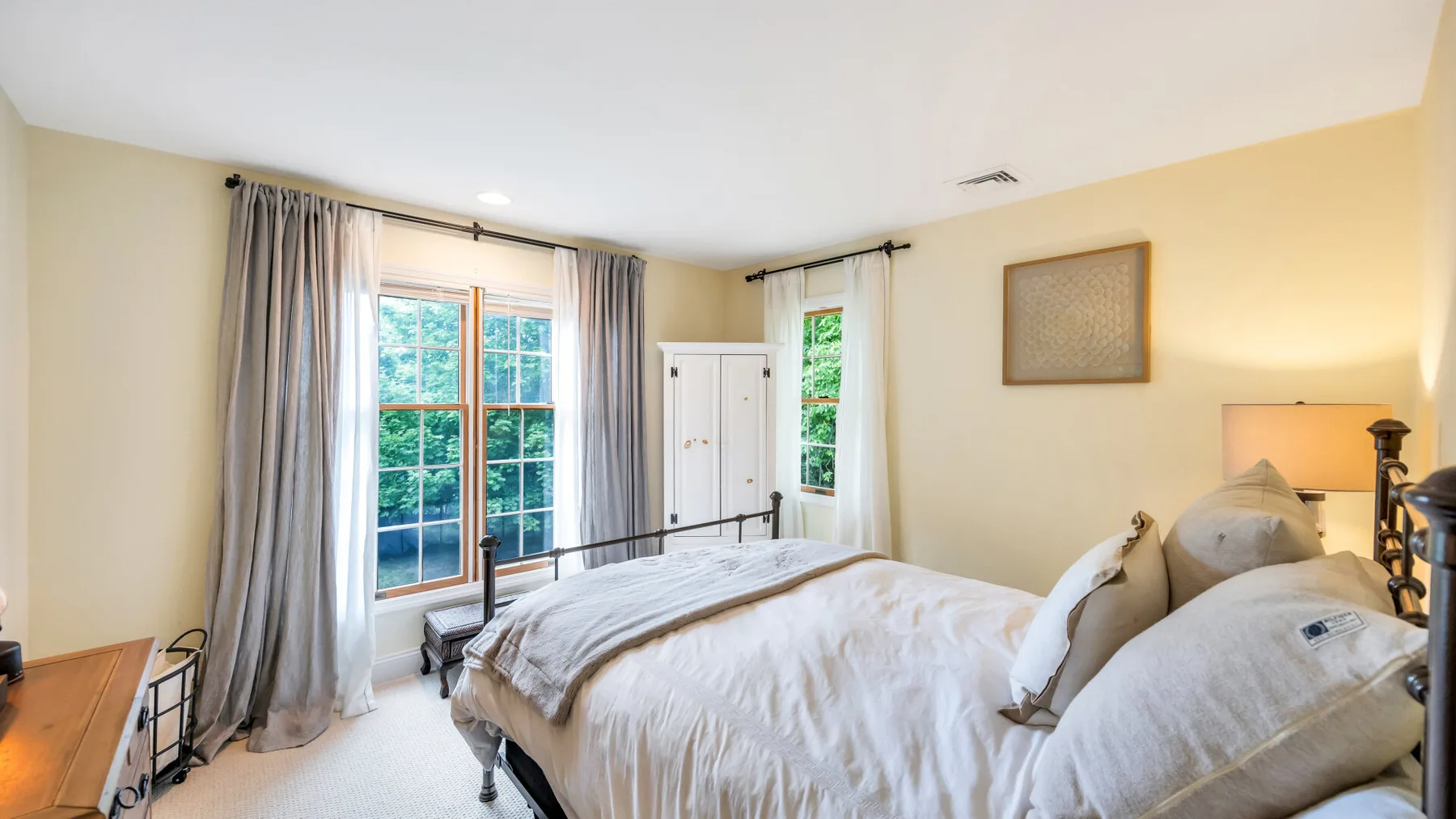 Un dormitorio con una cama junto a grandes ventanas y cortinas claras.